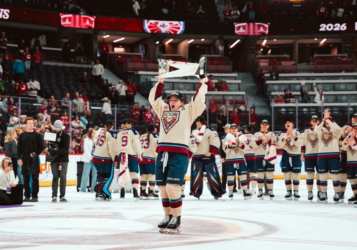 Kaitlin Willoughby holds up the Walter Cup in celebration on center ice in her Montreal Victoire uniform. Behind her cheering are her teammates. 