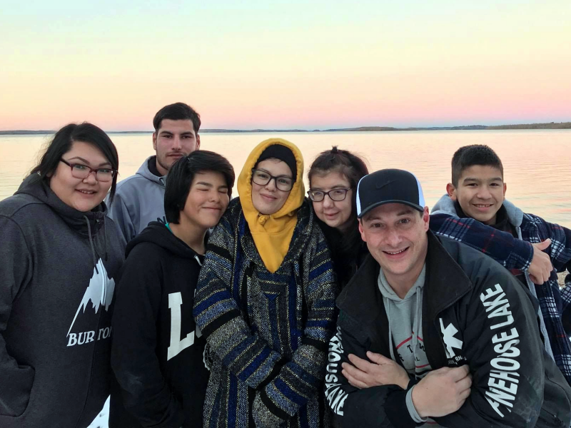Dre Erwin and six members of the Pinehouse Photography Club gathered together for a group photo in front of a lake at sunset.