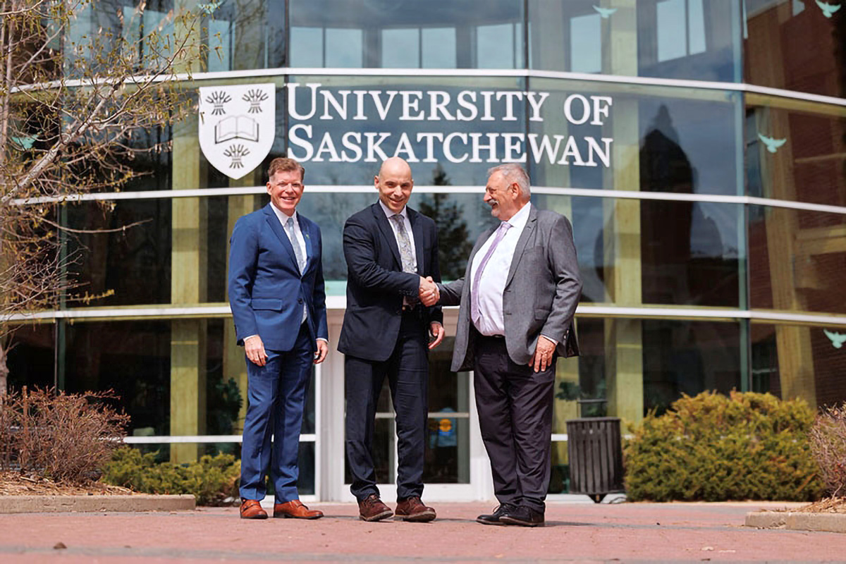 3 smiling men, Dr. Jay Wilson, principal of the USask Prince Albert campus, Dr. Vince Bruni-Bossio, president and vice-chancellor of USask, and Bill Powalinsky, mayor of the city of Prince Albert, stand outside of the Prince Albert Campus in front of the glass atrium with University of Saskatchewan logo, shaking hands.