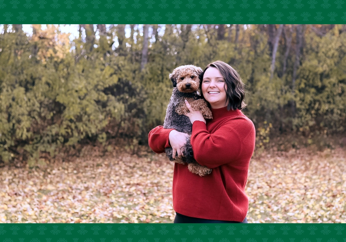 Brianna holding her dog, in front of a lush, fall forest.
